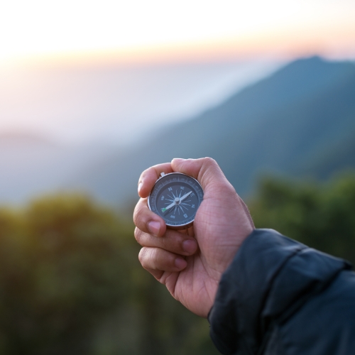 A man's hand infront of a distant view of a mountain holding a compass pointing east