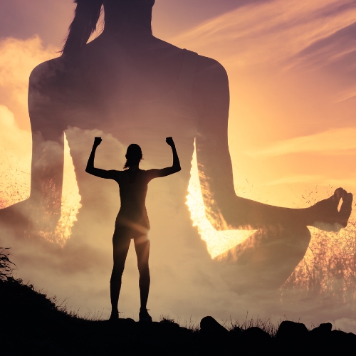 A woman standing triumphant infront of a sunset with a shadow of herself meditating behind her