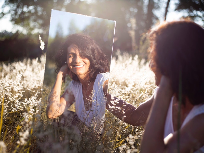 A woman who understands her human design improves her self-worth, looking at herself in the mirror, she is smiling because she is happy and truly loves herself